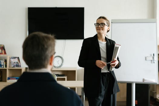 pexels-photo-6981013-6981013 Caucasian female teacher in black blazer holding books, presenting to a student in a classroom.
